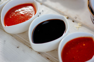 Different dips and sauces - red, white and black over white table.