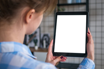 Over shoulder closeup view: woman hands holding digital tablet computer device with white blank screen in home interior. Mock up, copyspace, template, entertainment and technology concept 