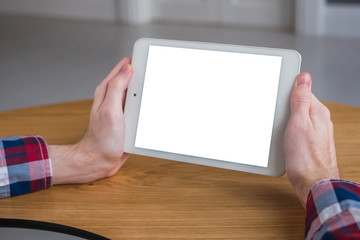 Man sitting at wooden table and looking at digital tablet computer device with white blank screen. Mock up, entertainment, copyspace, template, leisure time and technology concept