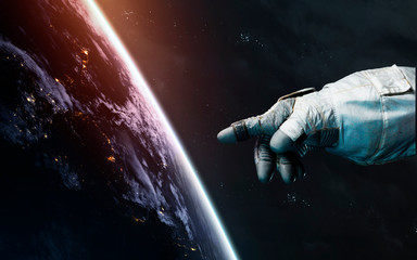 Astronaut hand points to Earth planet. Awesome science fiction render. Elements of this image...