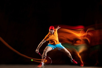 One caucasian man playing tennis isolated on black background in mixed light. Studio shot of fit...
