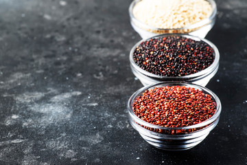 Black, white and red quinoa in bowls, raw quinoa groats assorted, gray kitchen table, selective focus