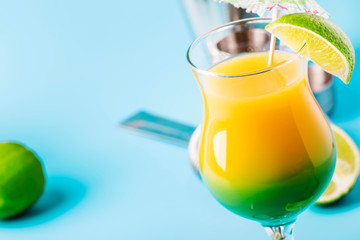 Two-layer alcoholic cocktail with mango juice, rum, liqueur, lime and ice, summer blue background, place for text