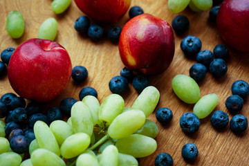 seasonal fruits. red nectarines, green grapes and blueberries on a light wooden background