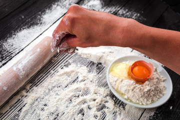 Women's hands roll out the dough on a black table sprinkled with flour.