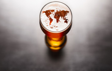 world map silhouette on foam in beer glass on black table. The continents shapes are altered ones from visibleearth.nasa.gov