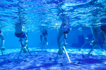 Tourists do water aerobics on exercise bikes in a tropical resort pool