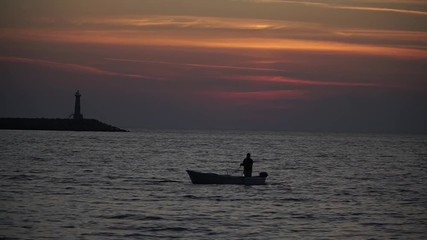 the silhouette of the boat is floating at sunset on the sea by the lighthouse