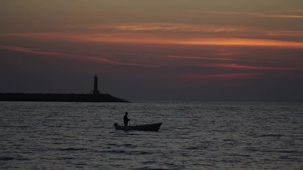 the silhouette of the boat is floating at sunset on the sea by the lighthouse