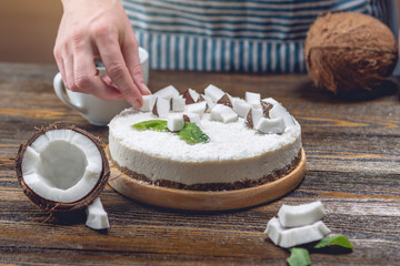 Confectioner decorates coconut raw cake with white pulp and mint. Healthy vegan dessert. Gluten and...