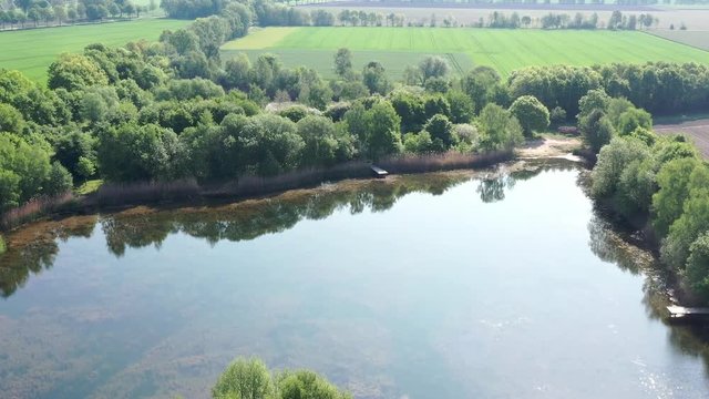Aerial photo with an overview of a small fishing pond at the edge of a large field, with the drone