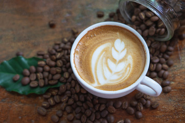 White coffee mugs and coffee beans Poured on a wooden table, beautifully arranged, decorated with coffee leaves. Is a mixture of raw materials for making coffee