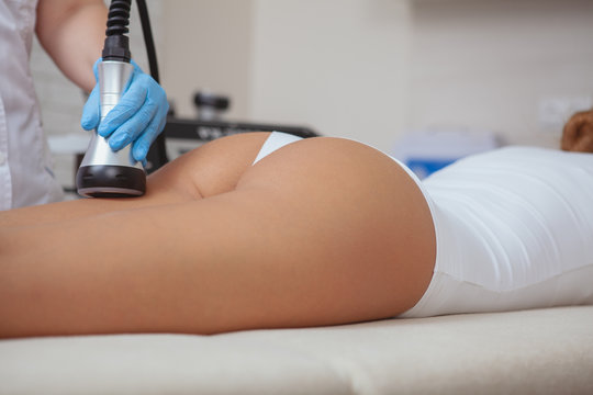 Woman With Perfect Sexy Buttocks Receiving Anti-cellulite Ultrasonic Treatment By Beautician. Cosmetologist Using Ultrasound Cavitation Machine On A Patient