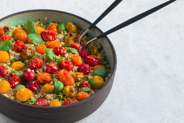 Quinoa, red roasted cherry tomatoes, orange roasted cherry tomatoes and yellow roasted cherry tomatoes, fresh basil salad with olive oil and balsamic in a pottery salad bowl. Side view, copy space