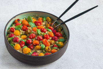 Quinoa, red roasted cherry tomatoes, orange roasted cherry tomatoes and yellow roasted cherry tomatoes, fresh basil salad with olive oil and balsamic in a pottery salad bowl. Side view, natural stone.