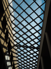 The construction is in the form of a grille under the glass roof of the mall, through which the blue sky is visible