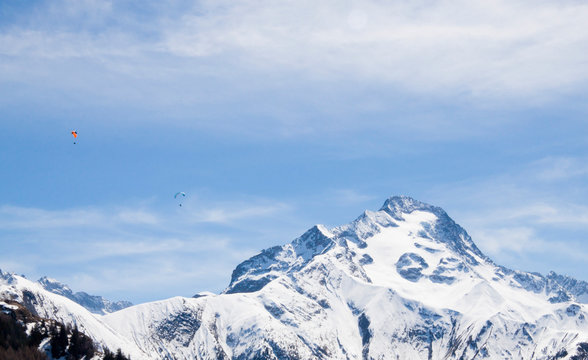 two parachutes flying in paralell in the sky over a snowed mountain