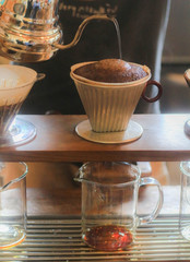 Manual drip (pour-over) coffee. Hand of barista pouring water on coffee ground. Coffee drips through beans and filters into several jar.