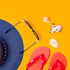 Summer beach sea accessories. Coral flip flops, blue straw hat, sunglasses, shells, starfish on yellow background top view flat lay copy space. Summer background. Holiday vacation travel concept.