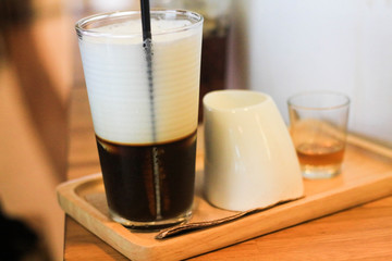 Glass of coffee jelly milk froth on top with glass of milk and syrup.