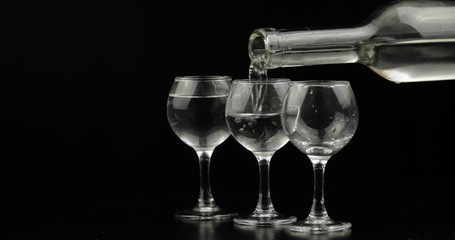 Pouring up shots of vodka from a bottle into glass against black background