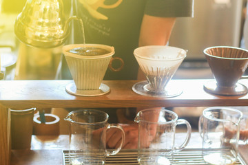 Manual drip (pour-over) coffee. Hand of barista pouring water on coffee ground. Coffee drips through beans and filters into several jar.