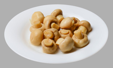 Marinated champignons on a white round plate. Light gray isolated background. Top side view. Close-up.