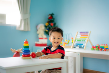 Adorable Asian Toddler baby boy sitting on chair and playing with color developmental toys at home..