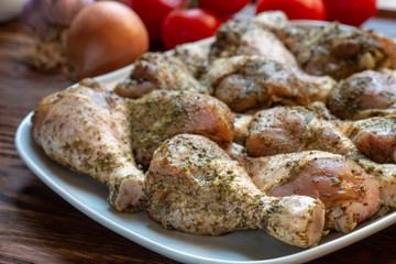 Raw chicken legs with herbs and spices on white dish.
