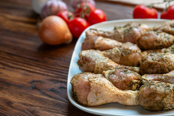 Raw chicken legs with herbs and spices on white dish.