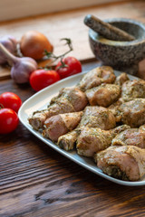 Raw chicken legs with herbs and spices on white dish.