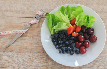 Fork and measuring tape with Healthy salad with Blueberries, Cherry and glass of tomato juice on wooden table. Food and health. Clean eating, dieting food concept.