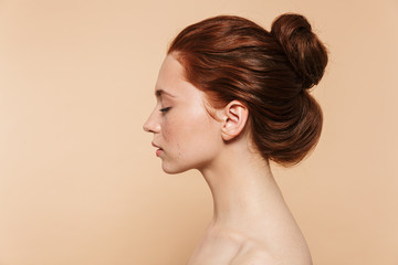 Young redhead woman posing isolated over beige wall background.