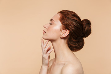 Young redhead woman posing isolated over beige wall background.