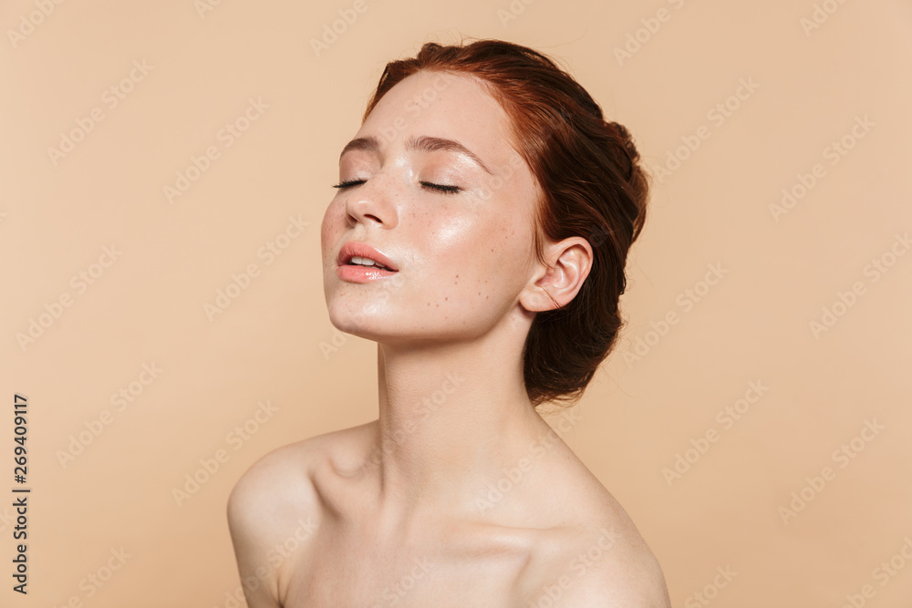 Wall mural young redhead woman posing isolated over beige wall background.