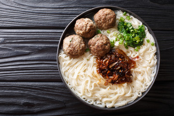 Traditional Indonesian beef meatball with noodles, fried onions, greens and broth close-up on a plate. horizontal top view