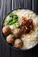 Bakso is Indonesian meatball served with noodles, served with caramelized onions and herbs close-up on a plate. Vertical top view