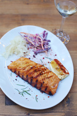 Delicious grilled salmon fish steak served with seasonings, veggies and lemon on a white plate on a wooden table. Restaurant menu design. Barbecue party. 