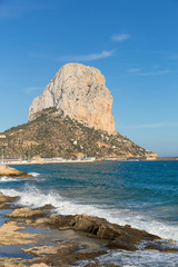Fototapeta na wymiar Calp Spain Penon de Ilfach landmark rock Costa Blanca in portrait with blue sky and waves