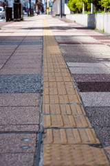 Obraz premium Bright yellow tactile footpath for people who have visually impaired on the walkway. This path will guide blind people walking safely in a busy city.