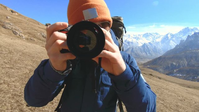 Portrait of a happy bearded traveler photographer in sunglasses and a hat with a reflex camera in his hands and taking pictures against the background of the mountains. Photo travel concept