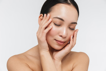 Portrait of tranquil half naked asian woman touching her clear skin with her eyes closed