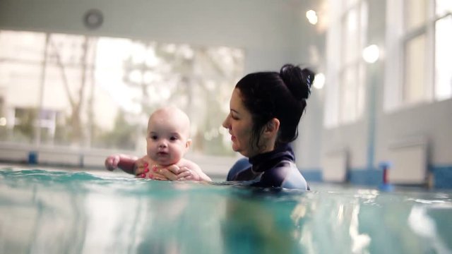 Female trainer or mother teach a little todler to dive under the water. Holds him above the water then dive together under water. Footage above and below the water