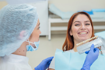 Check and select the color of the teeth in the dentist chair. Dentist makes the process of treating a beautiful young red-haired girl. Selection of a tooth implant.