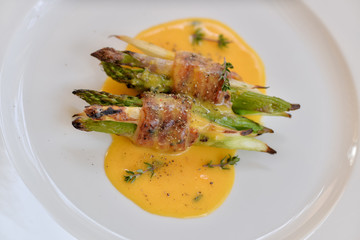 asparagus wrapped in grilled bacon with sauce on a white plate