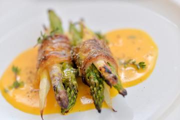 asparagus wrapped in grilled bacon with sauce on a white plate