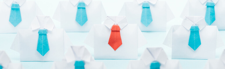 panoramic shot of origami white shirts with blue ties with one red on blue background, think different concept