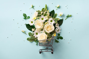Shopping trolley with flowers on blue pastel background. Banner with copy space. Top view, flat...