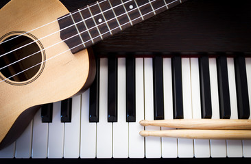 Ukulele with drum sticks on piano. Top view with copy space.