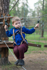 A little boy is training in a rope park. The child climbs the obstacle course. Active recreation in the park in the fresh air.